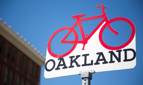 Sign for Oakland with a red cut-out bike on top and blue sky background. 