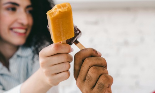 A woman is cheering a popsicle with a man also cheering a popsicle to her. 